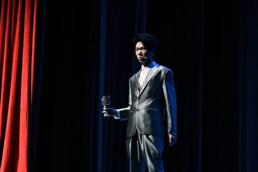 An alumnus performing on the red-curtained stage during the anniversary evening