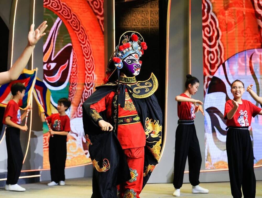A Peking opera performer in full painted-face costume with younger pupils in red