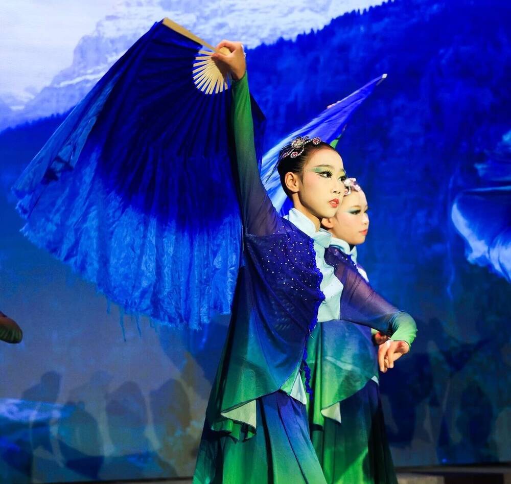 A dancer in blue sleeves with a fan, mid-movement in the dance A Great River