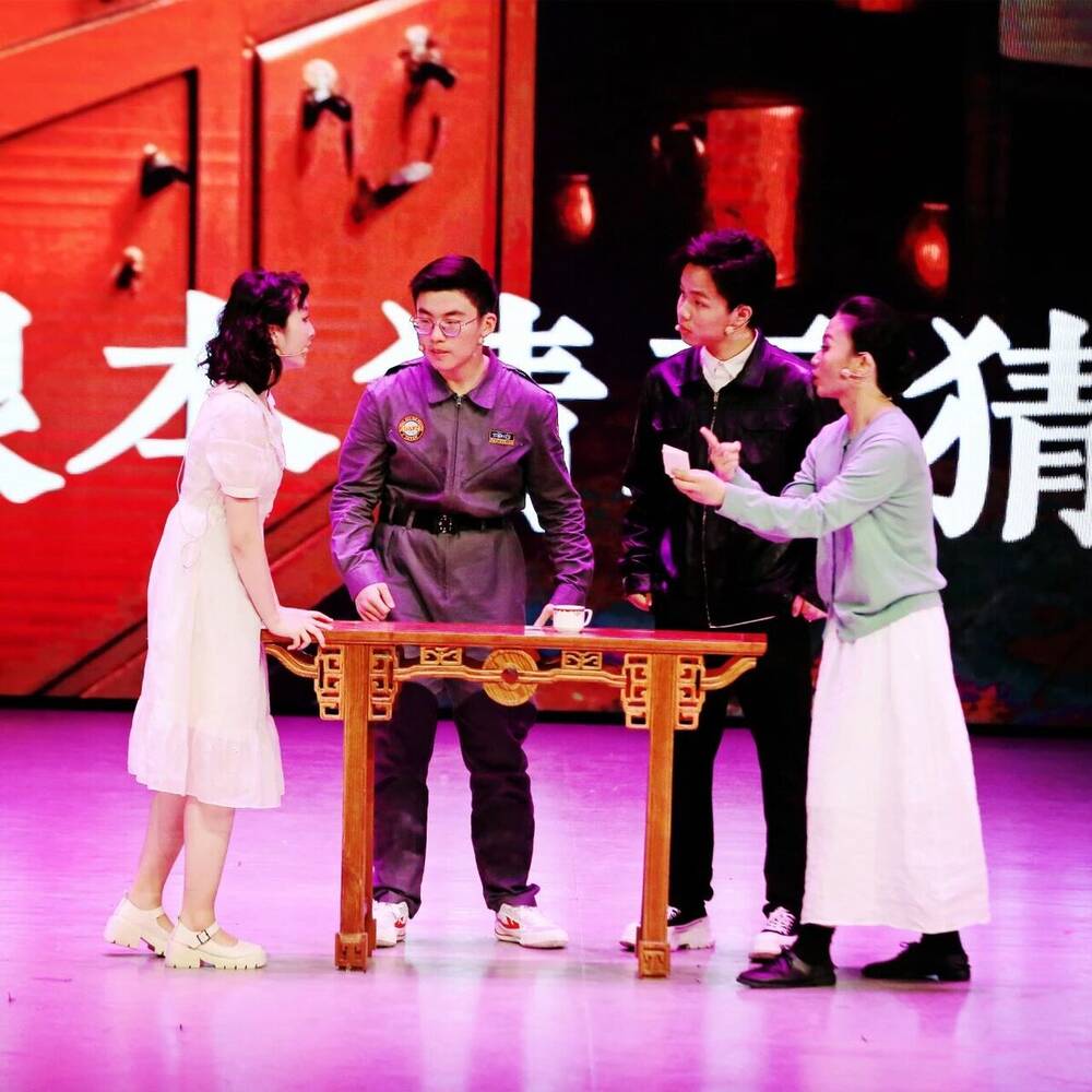 Three performers at a table in a brightly lit scene from Lucky Stiff