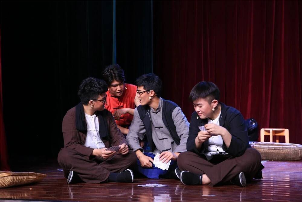 Four students seated on the floor of a dark stage during a scene