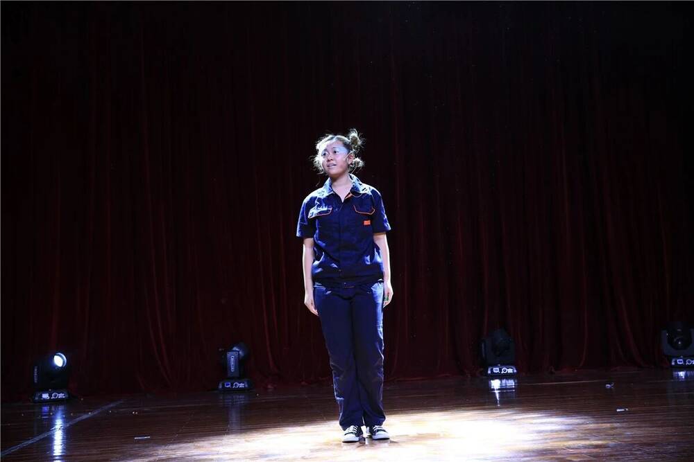 A single performer standing alone in a pool of light on a dark stage