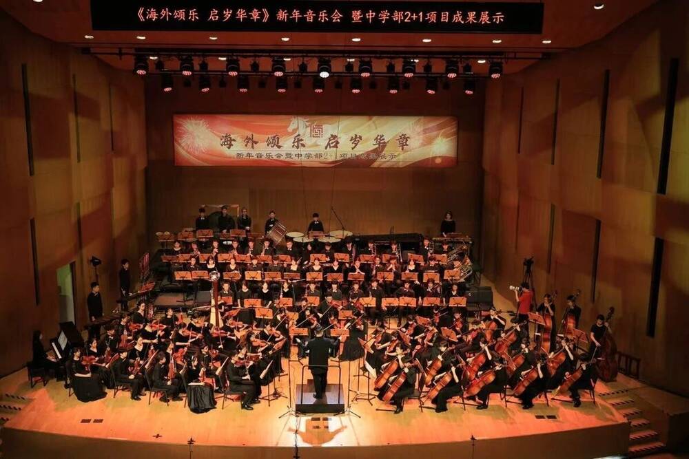 The orchestra and choir on stage beneath a banner at a school concert hall
