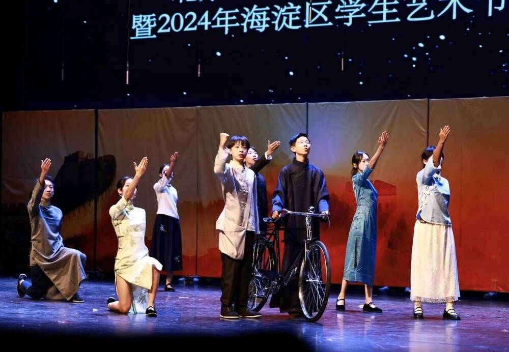 A staged scene with a bicycle and a large ensemble on a school stage