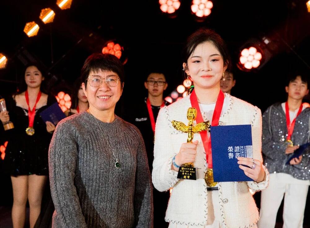 The winner holding a trophy and certificate on stage with other finalists