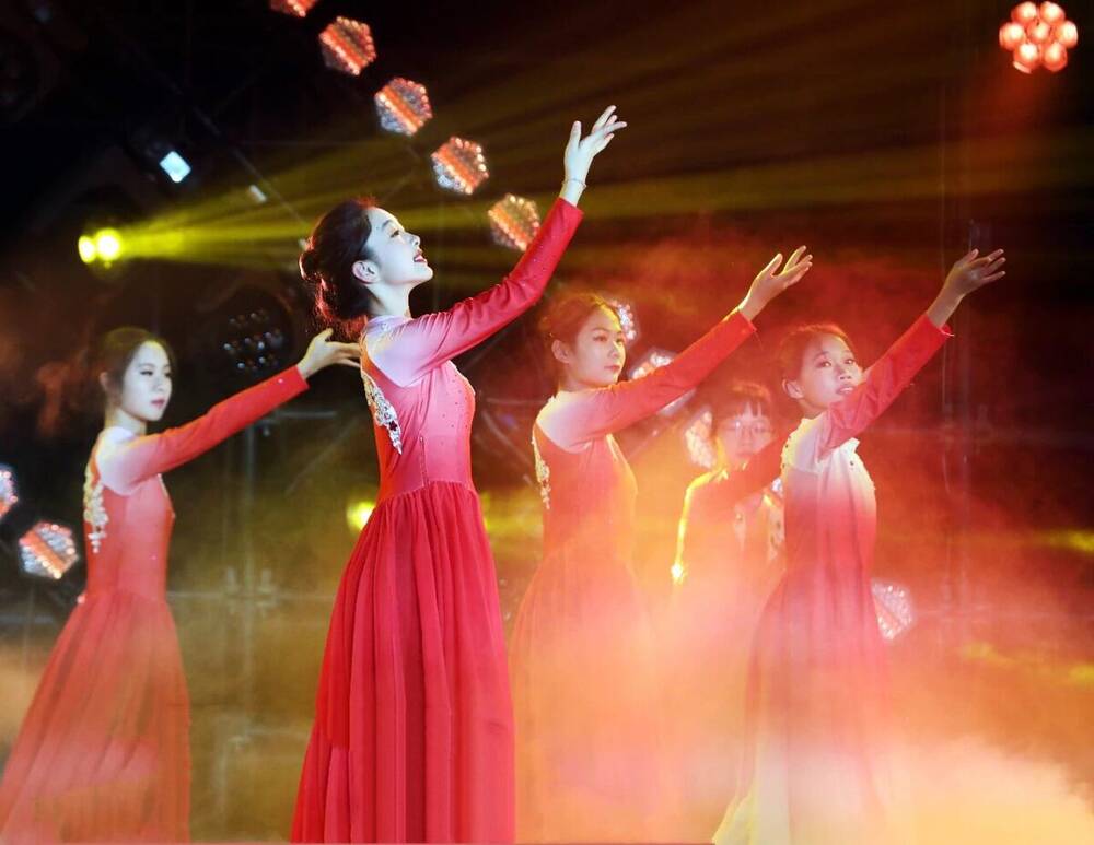 A singer in a white gown performing with dancers in red dresses