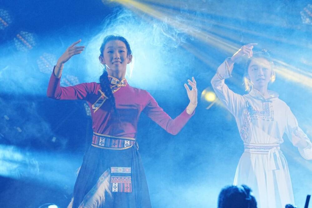 A performer in Mongolian dress on stage with dancers in blue light