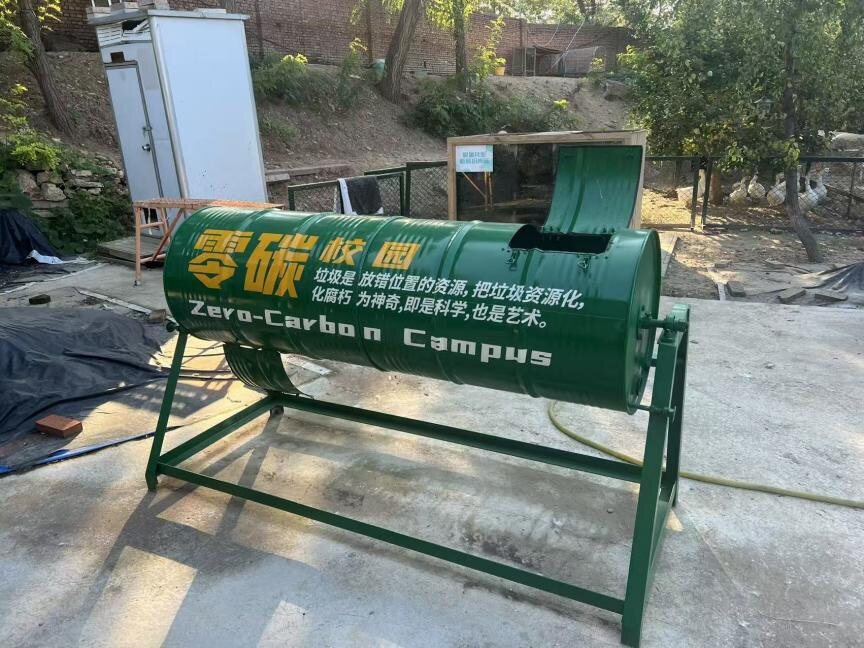 A green rotary drum composter labelled Zero-Carbon Campus standing on the school farm