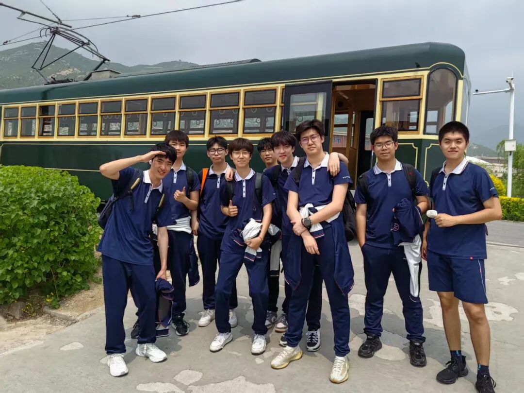 Students in sports kit beside a vintage green tram during a school trip