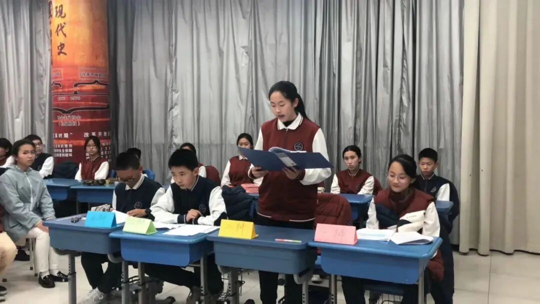 Students seated at desks during a classroom debate, with a speaker at the front