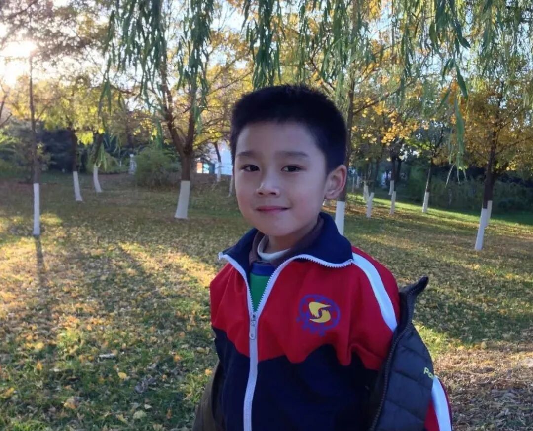 A boy in a school tracksuit standing among autumn trees in a park
