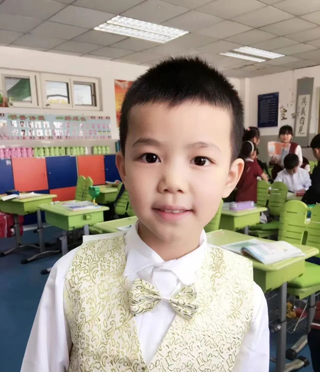 A young boy in a waistcoat standing in a primary school classroom
