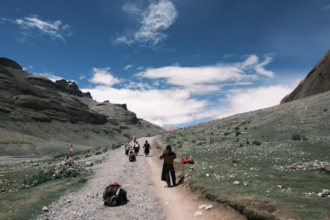 A group of walkers following a mountain trail beneath a wide sky