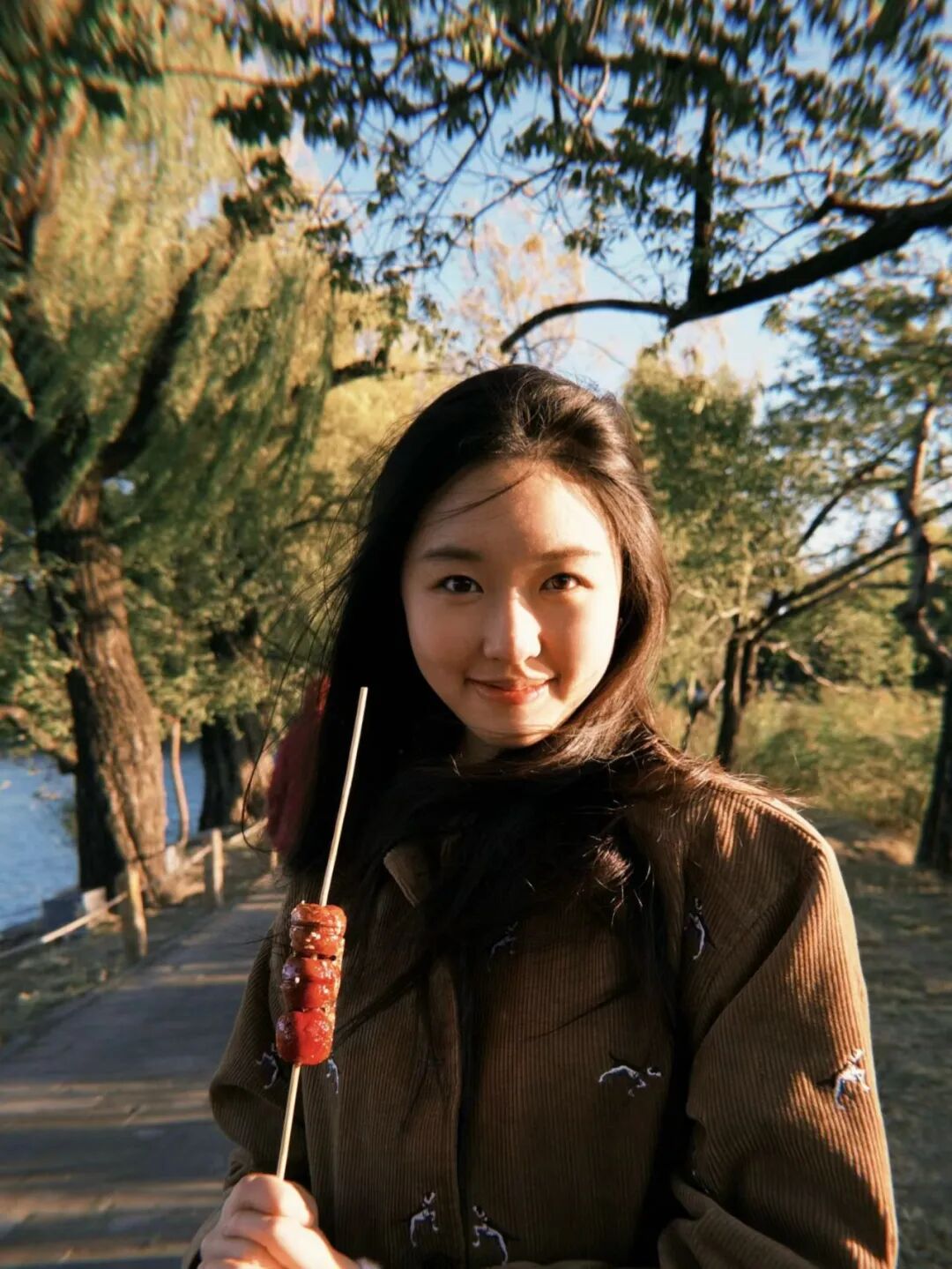 Zhou Zhuoyi standing outdoors in a brown coat holding autumn leaves