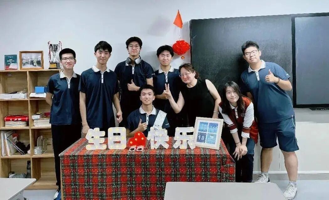 Ma Liangyu with classmates and a teacher around a birthday cake in a classroom