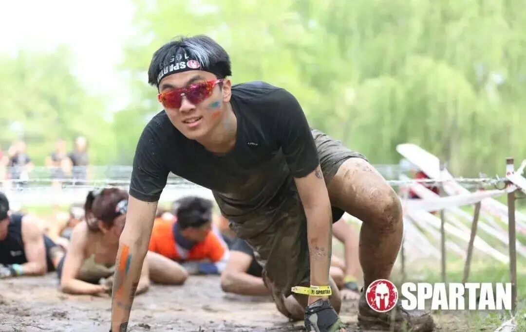 Ma Liangyu crawling under wire on a muddy Spartan Race course