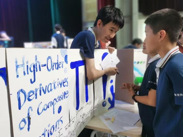 A student explaining his High-Order Derivatives of Composite Functions poster to a visiting peer at the exhibition