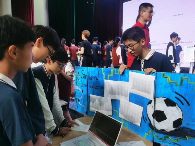 Visiting students reading a poster on simulated football trajectories, with the project laptop open in front of it