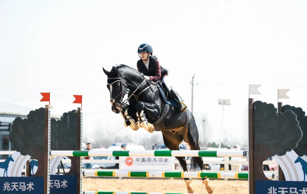 A rider and horse clearing a fence at an outdoor competition