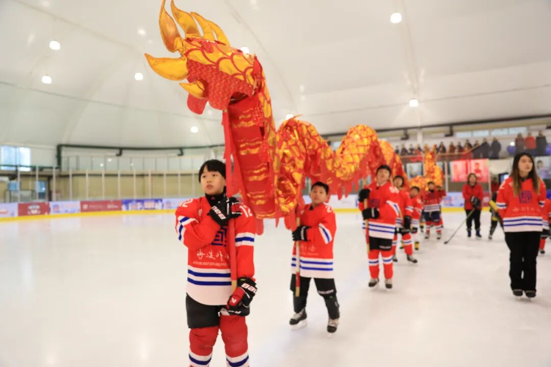 A procession of young hockey players carrying a dragon puppet across the ice