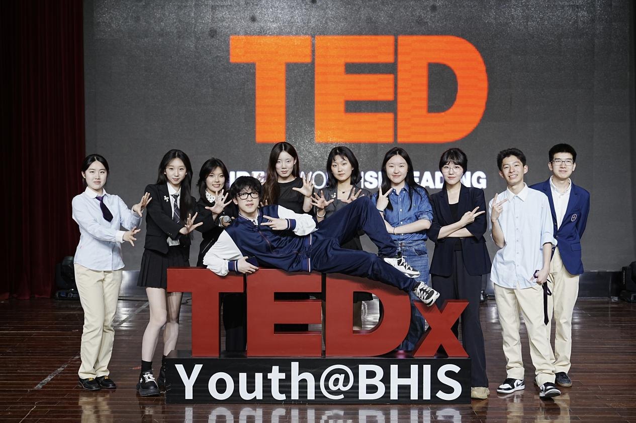 The 2024 TEDx Youth@BHIS team posing with the TEDx sign in front of the TED backdrop