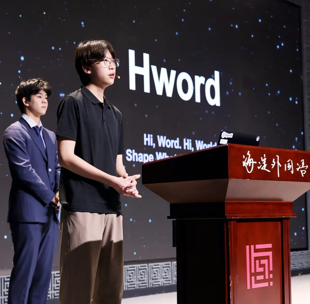 Two students on stage at the vocabulary learning project launch, in front of an Hword screen